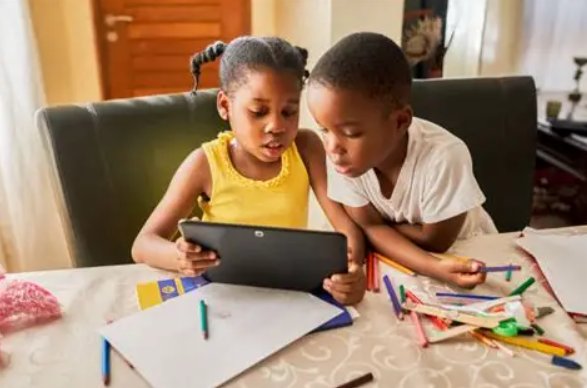 Two young siblings working through schoolwork together on a tablet at home